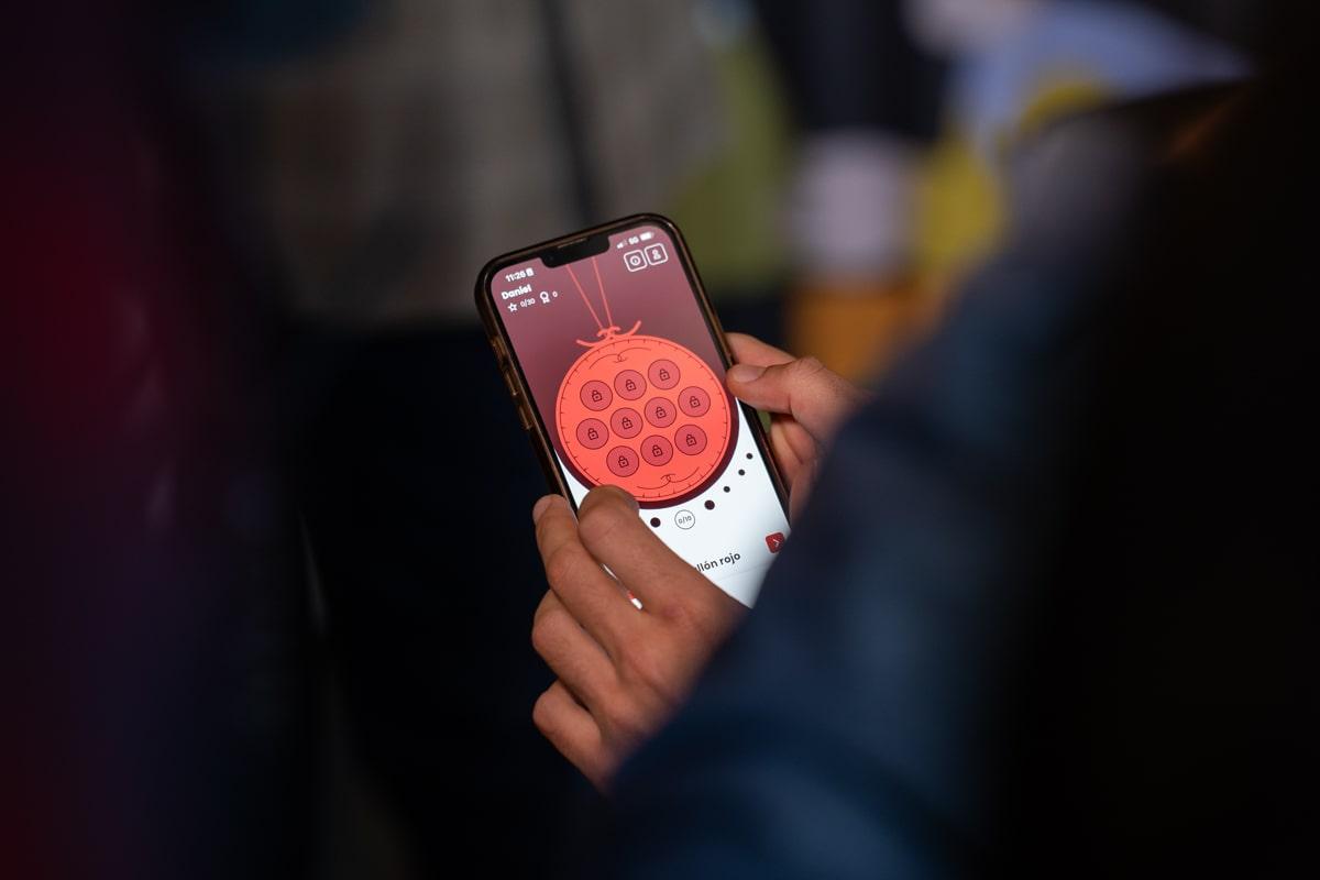 Una persona sostiene un móvil en el que aparecen los medallones de la app La Hermandad de Las Palabras